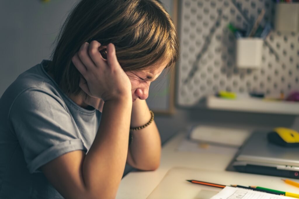 Upset schoolgirl struggling with homework while studying at a desk, showing stress and learning difficulties in children.